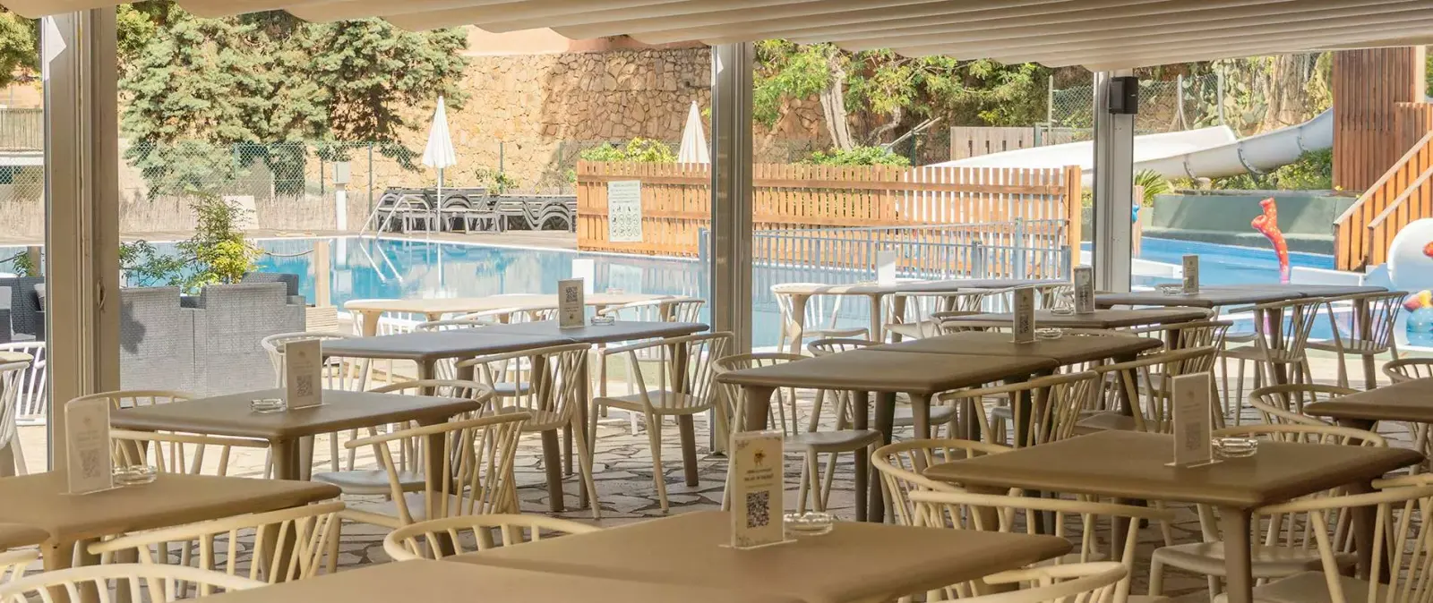 Overdekt terras van de bar met houten tafels, met uitzicht op het zwembad