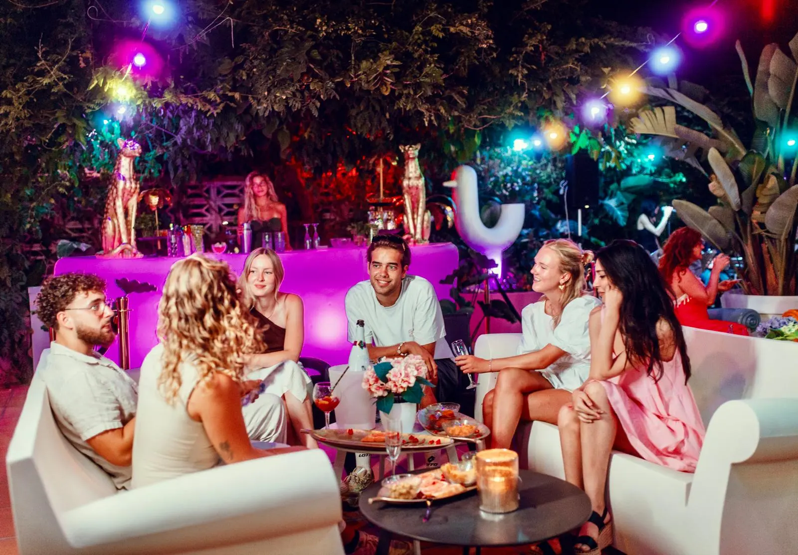 Het cocktailterras van de camping ’s avonds, met witte loungebanken onder lichtslingers